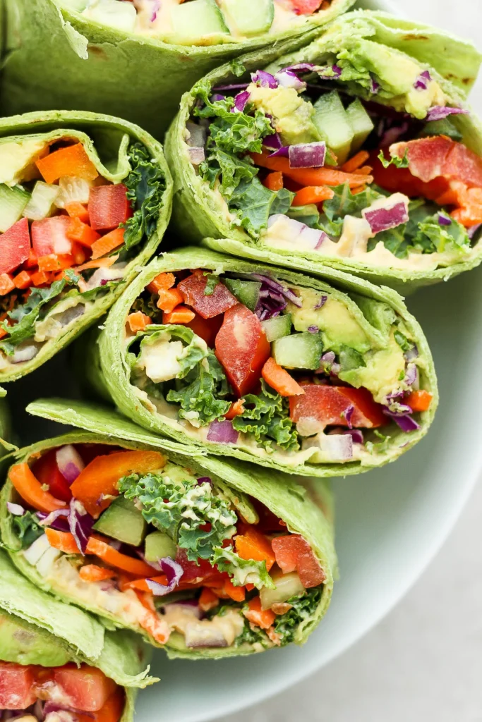 Close-up of vibrant vegetable wraps filled with fresh kale, tomatoes, carrots, avocado, and red cabbage in green tortillas