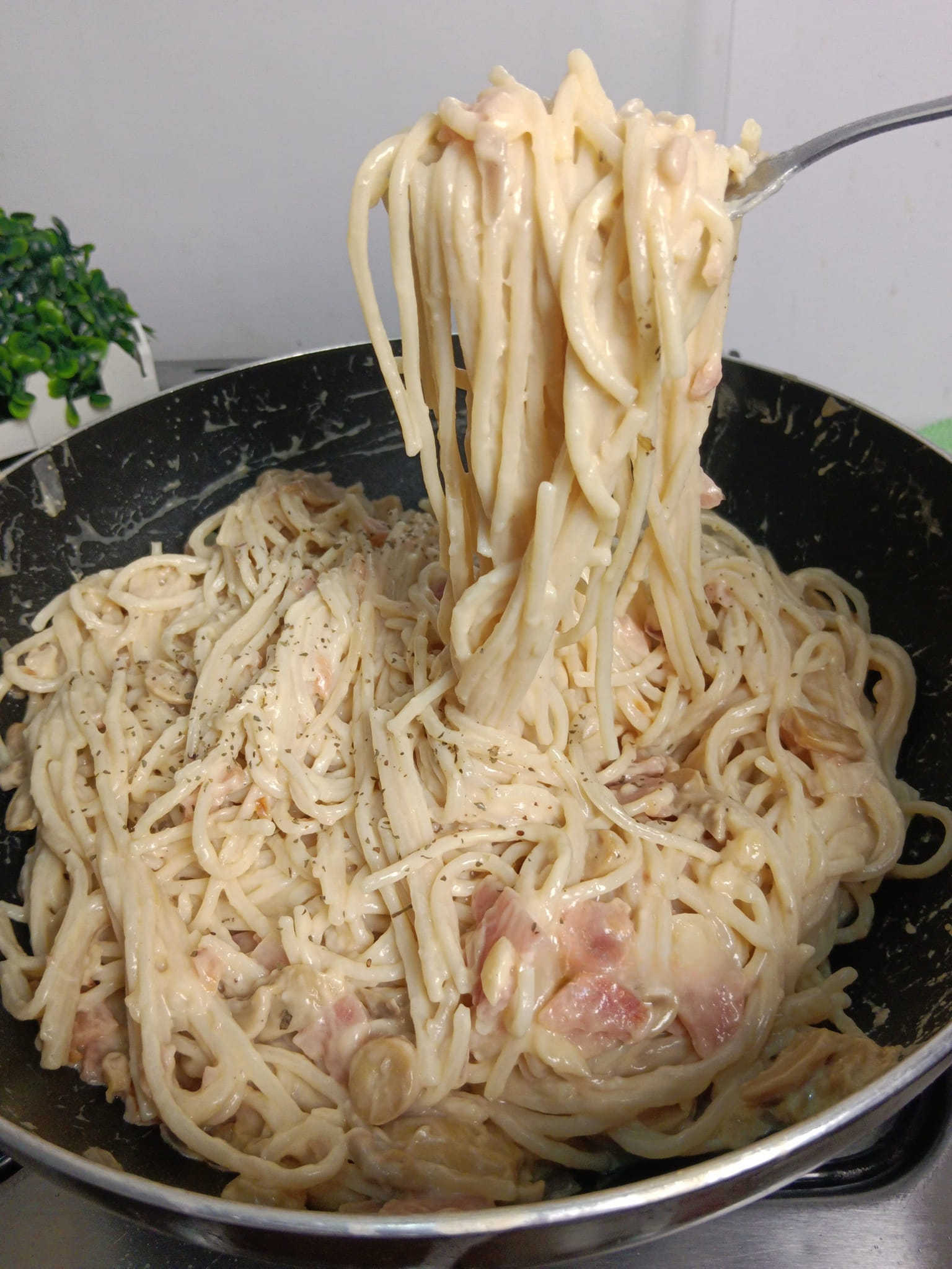 Close-up of creamy Carbonara pasta with ham and mushrooms in a skillet