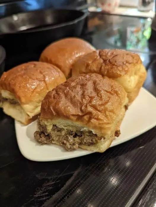 A plate of freshly baked Maid-Rite sliders with glossy buns and visible juicy meat filling, served on a white plate