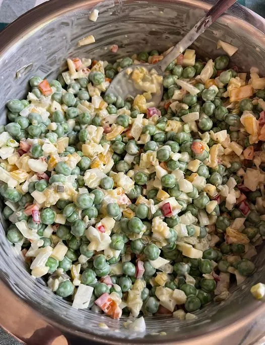 Creamy green pea salad with chunks of cheese and colorful vegetables in a glass mixing bowl