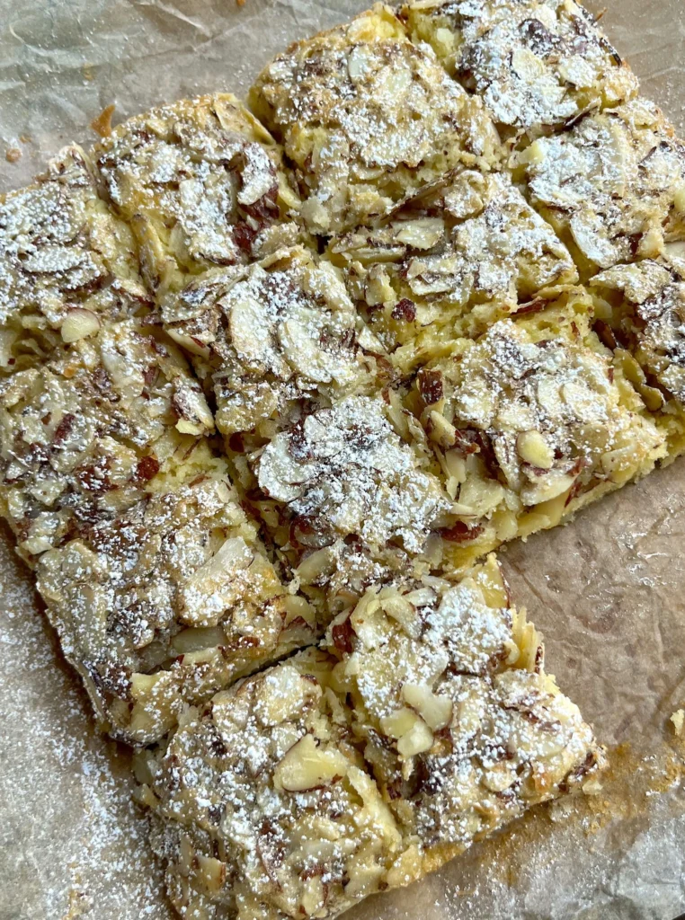 Homemade Swedish Visiting Cake sliced into squares, topped with sliced almonds and dusted with powdered sugar on parchment paper