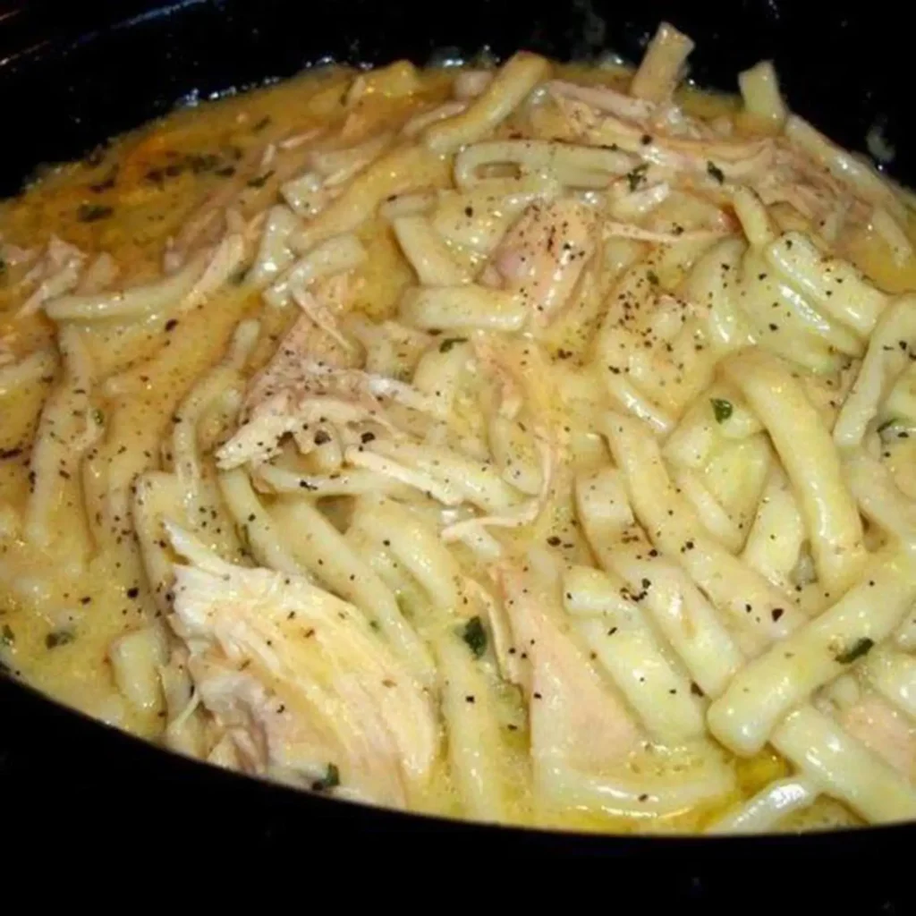 Creamy chicken and noodles in a black slow cooker, sprinkled with herbs and black pepper