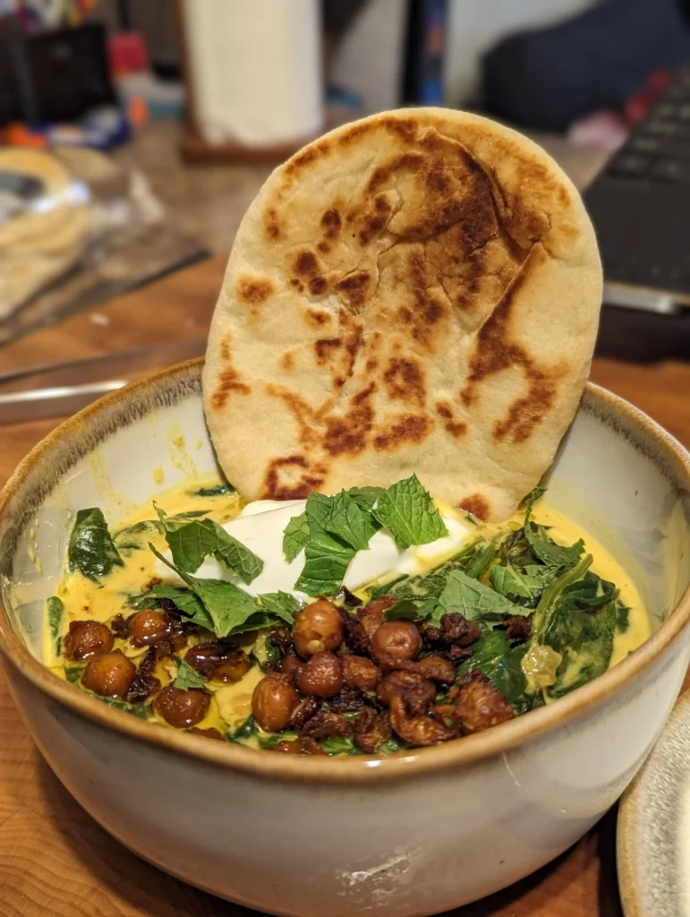  Bowl of coconut chickpea stew with crispy chickpeas, fresh mint, and naan bread