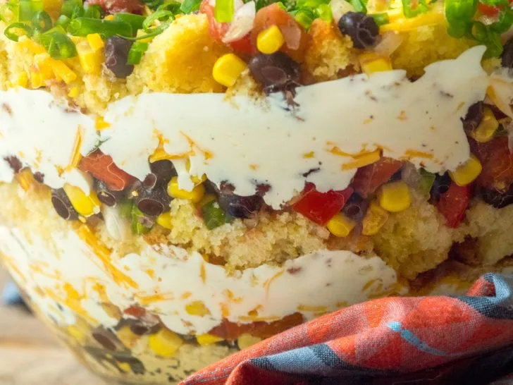 Close-up of a layered Cowboy Trifle with cornbread, vegetables, beans, and creamy dressing in a glass bowl