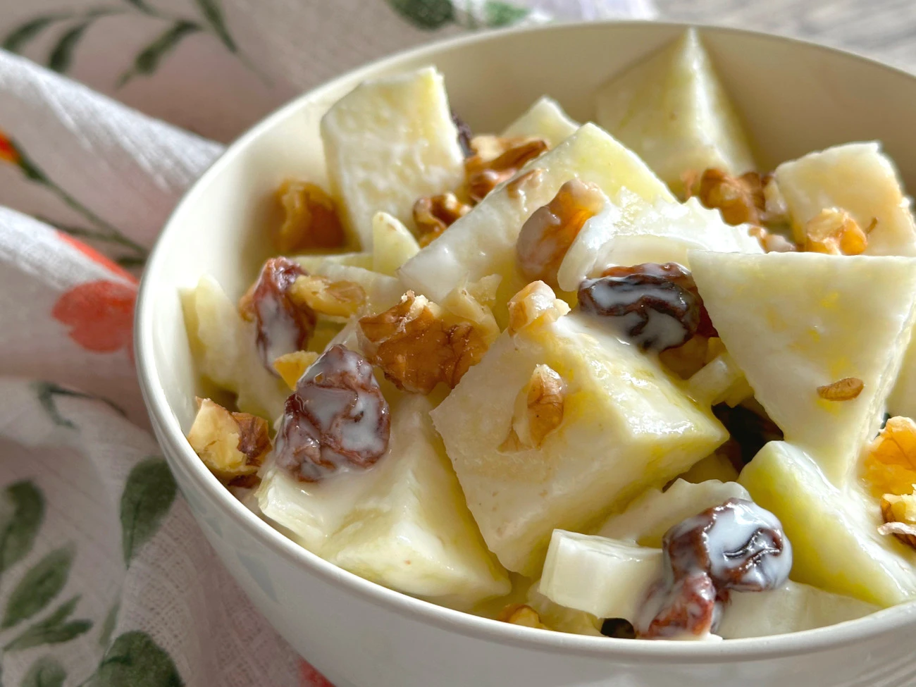 Creamy apple salad with chunks of crisp apples, nuts, and dried fruit in a white bowl