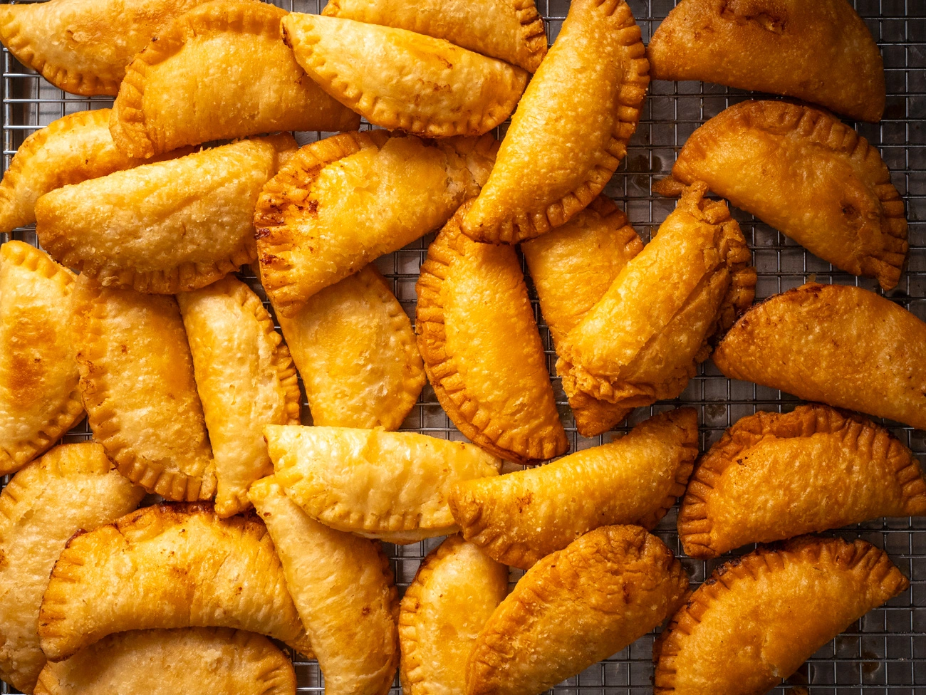 Freshly baked golden potato empanadas on a wire cooling rack