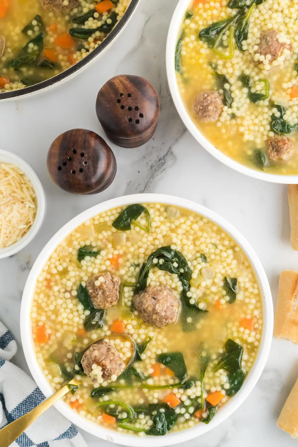 Italian Wedding Soup with meatballs, acini di pepe pasta, spinach, and carrots in white bowls