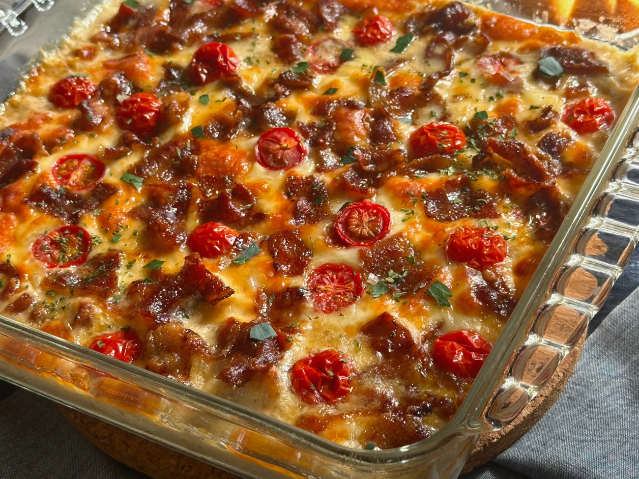 Baked Kentucky Hot Brown Dip with melted cheese, crispy bacon bits, and roasted cherry tomatoes in a glass baking dish