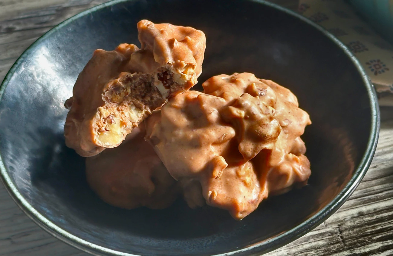 Freshly made New Orleans pecan clusters in a dark blue ceramic bowl on a rustic wooden surface